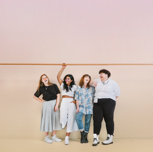 Four smiling young adults wearing colorful sunscreen on their noses against a light pink background.